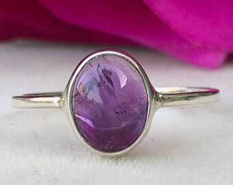 May include: A silver ring with a purple amethyst gemstone. The ring is set in a simple band and the stone is oval shaped.