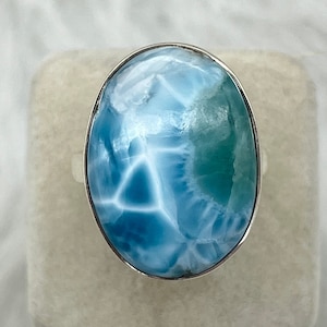 Könnte beinhalten: Ein silberner Ring mit einem ovalen, blau-grünen Edelstein. Der Edelstein hat ein wirbelndes Muster.