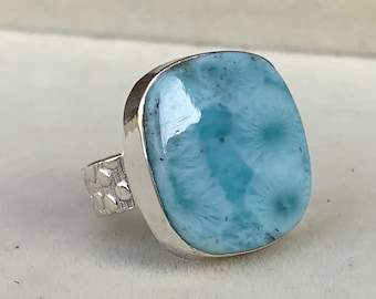 May include: A silver ring featuring a light blue gemstone. The gemstone is square-shaped with rounded edges. The ring band has a textured finish with small dots.