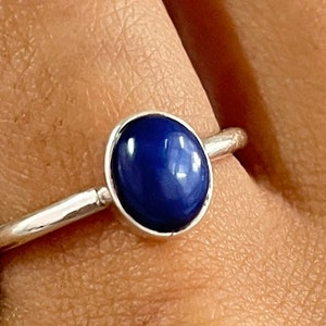 Może przedstawiać: Srebrny pierścionek z owalnym, ciemnoniebieskim kamieniem.