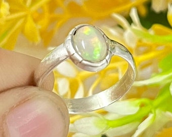 May include: A silver ring with a white opal gemstone. The ring is set in a simple band and the opal is oval shaped.