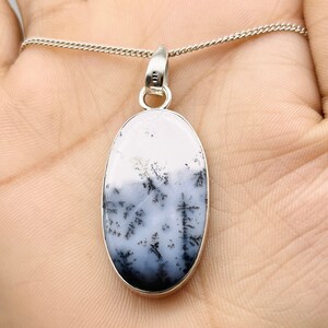 May include: Oval pendant on a silver chain. The pendant has a white and grey stone with a black tree-like design. The pendant is set in a silver bezel.