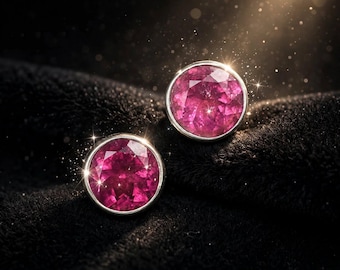 Puede incluir: Un par de pendientes de botón redondos con piedras preciosas facetadas de color rosa intenso engastadas en biseles de metal plateado pulido. Las piedras circulares muestran un corte brillante con múltiples superficies reflectantes.