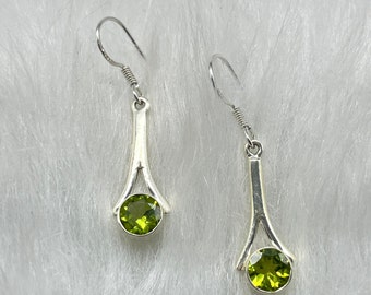 Puede incluir: Un par de pendientes de plata con detalles de piedras preciosas verdes. Los pendientes tienen un diseño simple y elegante con un colgante en forma de lágrima.