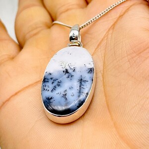 May include: Silver chain necklace with an oval pendant. The pendant has a white and grey stone with a dendritic pattern, like a landscape. The stone is set in a silver bezel.
