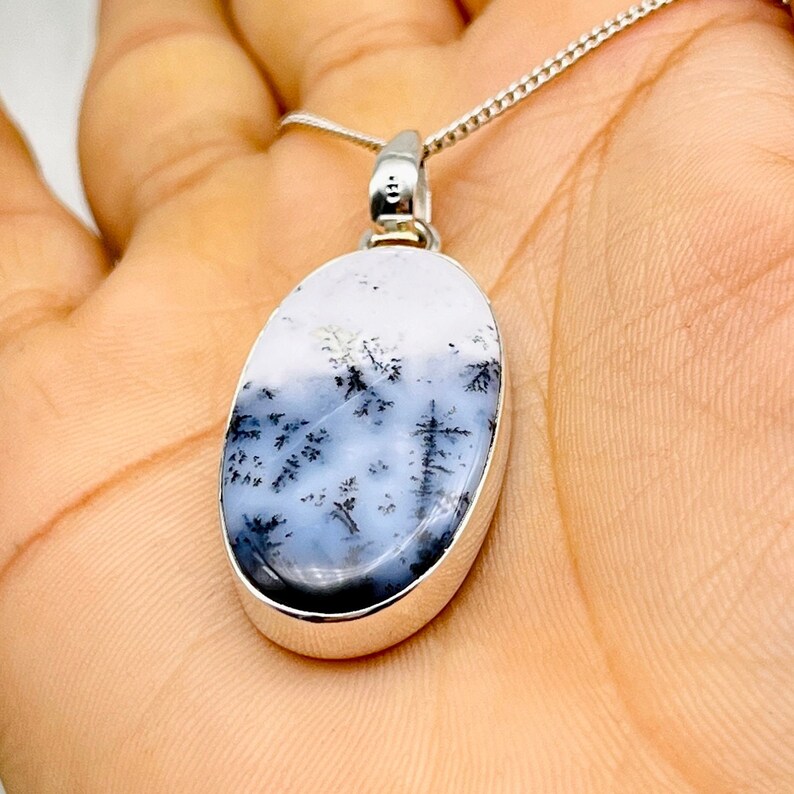 May include: Silver chain necklace with an oval pendant. The pendant has a white and grey stone with a dendritic pattern, like a landscape. The stone is set in a silver bezel.