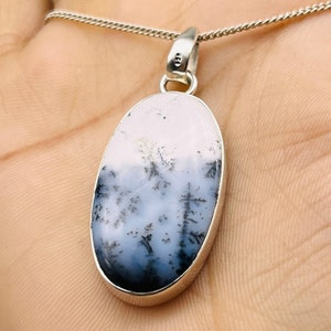 May include: Oval pendant necklace with a silver chain. The pendant features a dendritic agate stone with a landscape-like pattern in shades of white, grey, and black. The stone is set in a silver bezel.