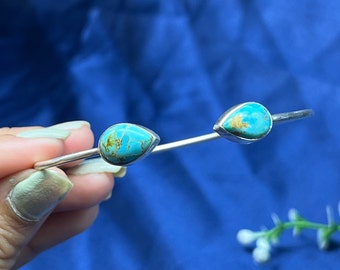 May include: A silver bangle bracelet with two turquoise teardrop-shaped stones.
