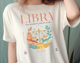 Può includere: Una t-shirt bianca con un design grafico che presenta il segno zodiacale Bilancia. Il design include una bilancia, foglie e il testo "Bilancia, Il Settimo Segno Zodiacale, Armonia, Equilibrio, Segno d'Aria, 09 23 - 10 23".
