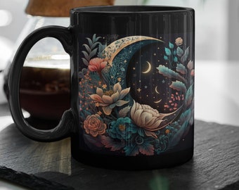 May include: Black ceramic mug featuring a crescent moon design surrounded by flowers and stars. The moon is gold and the flowers are in shades of pink, blue, and green.