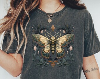May include: A dark gray t-shirt with a graphic of a large, yellow and green butterfly with floral accents. The butterfly has a detailed design and is surrounded by small flowers and leaves.