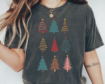 Puede incluir: Una camiseta gris oscuro con un gráfico de nueve árboles de Navidad estilizados en varios colores, incluyendo rojo, verde, marrón y rosa. Los árboles están decorados con estrellas, luces y espirales.