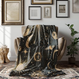 Könnte beinhalten: Eine schwarze Decke mit einem goldenen Sternenhimmelmuster mit Monden, Sternen und Planeten. Die Decke liegt über einem braunen Sessel.