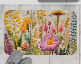 May include: A colorful bath mat with an embroidered floral design featuring pink, yellow, and blue flowers. The flowers are arranged in a bouquet-like pattern on a white background.