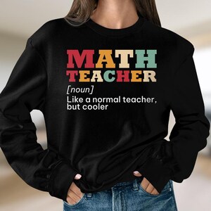 May include: Black long-sleeved sweatshirt with the text "MATH TEACHER [noun] Like a normal teacher, but cooler" in colourful retro-style lettering.