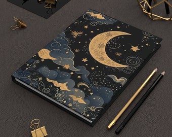 May include: A black notebook with a gold crescent moon and stars design. The notebook has a textured cover and a gold border.