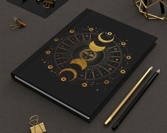 May include: A black notebook with a gold foil design of a sun and moon phases. The design is surrounded by stars and other celestial symbols.
