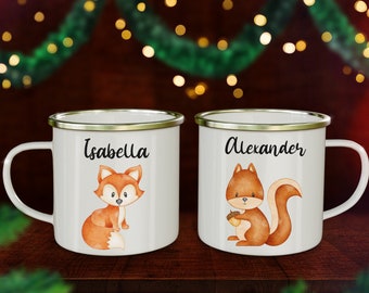 Könnte beinhalten: Zwei weiße Emaille-Tassen mit silbernen Rändern und Griffen. Eine Tasse zeigt eine Fuchsgrafik und den Namen "Isabella". Die andere Tasse hat eine Eichhörnchen-Illustration und den Namen "Alexander".
