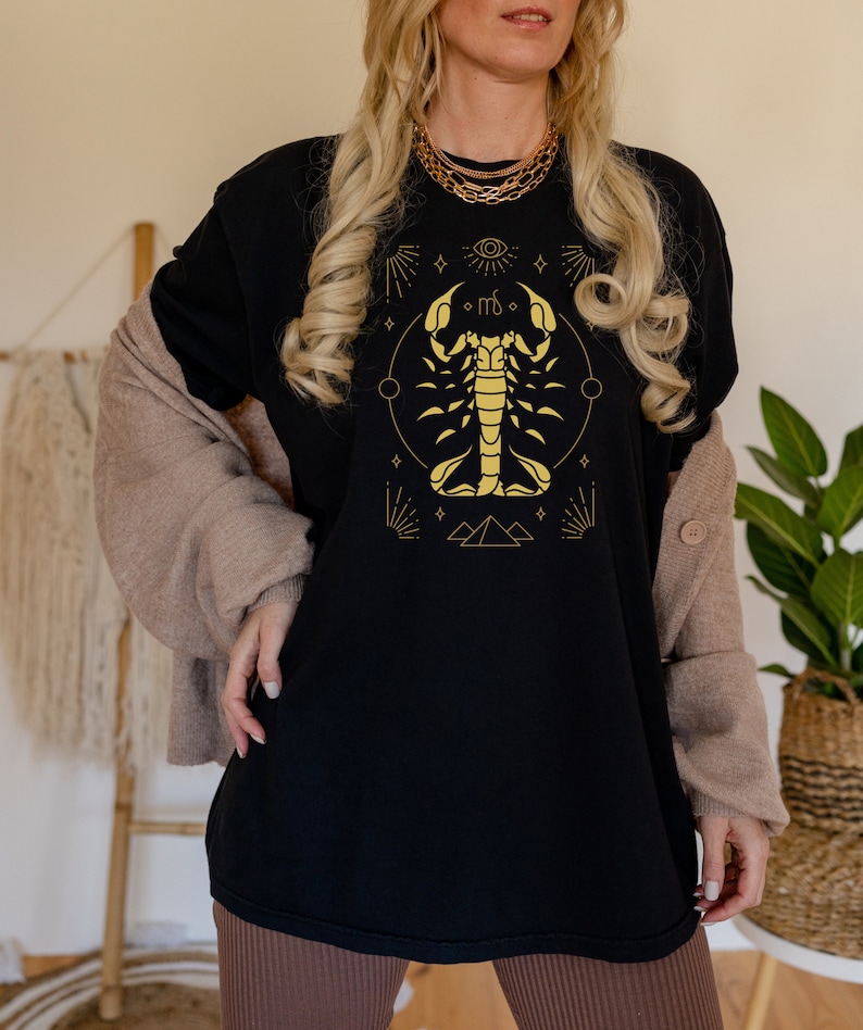 May include: Black t-shirt with a gold scorpion zodiac symbol and other astrological symbols. The scorpion is surrounded by a circle with stars and a crescent moon.