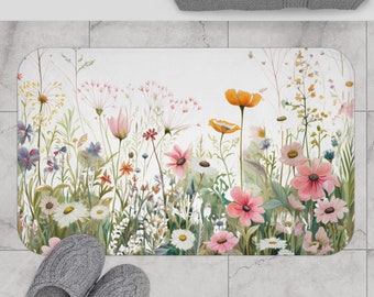 May include: A white bath mat with a floral design featuring pink, yellow, and green flowers. The flowers are arranged in a row across the mat, with the stems extending up towards the top of the mat.
