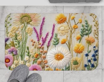May include: A white bath mat with an embroidered floral design featuring various flowers in shades of pink, yellow, green, and blue.