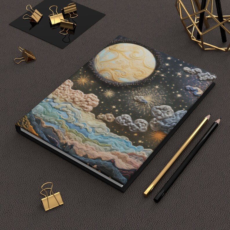May include: A black notebook with a colorful, embroidered design of a moon, stars, and clouds. The design is reminiscent of a night sky.