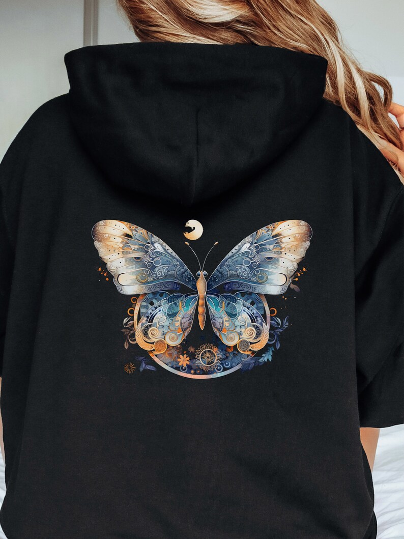 Pode incluir: Moletom preto com um design detalhado de borboleta nas costas. A borboleta tem asas azuis, douradas e brancas com padr&otilde;es intrincados. Uma pequena lua est&aacute; acima da borboleta, dentro de uma moldura circular.