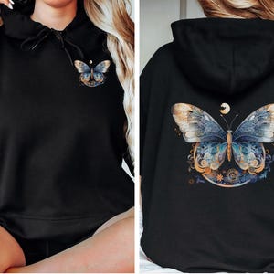 Pode incluir: Moletom preto com design de borboleta. A frente do moletom tem uma pequena borboleta. A parte de tr&aacute;s do moletom exibe uma borboleta maior com detalhes azuis, dourados e brancos. H&aacute; uma lua acima.