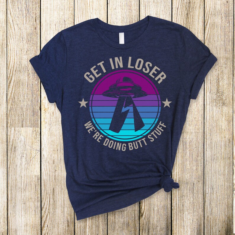 May include: A navy blue t-shirt with a retro-style graphic of a UFO and the text "Get in loser, we're doing butt stuff".