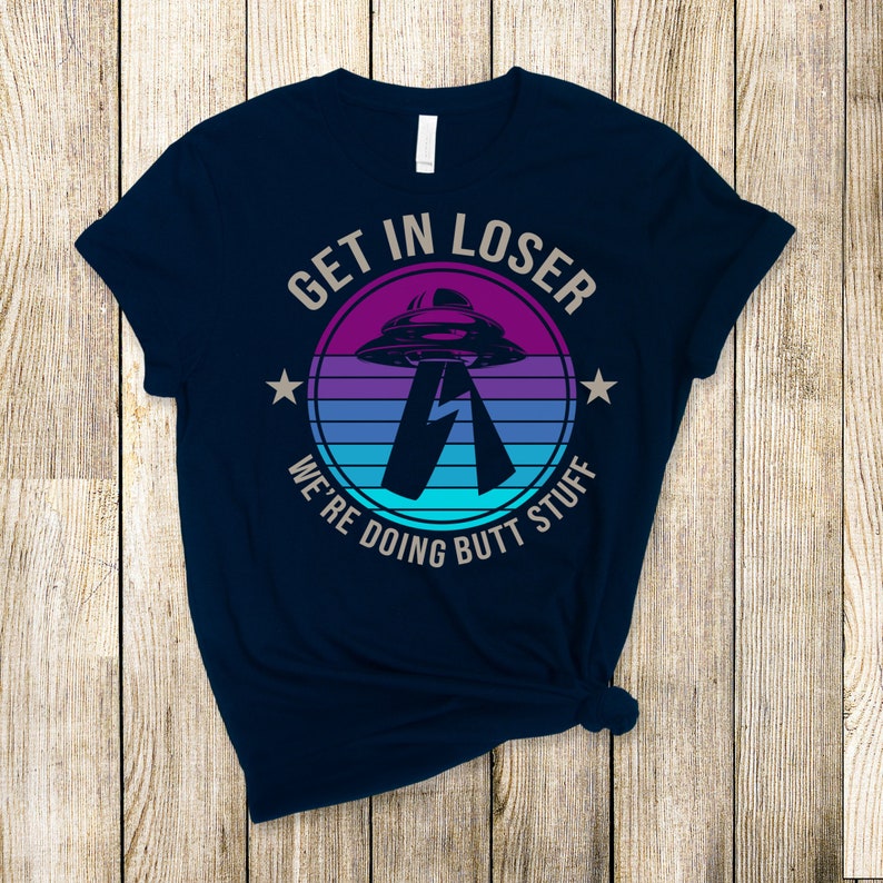 May include: Navy blue t-shirt with a retro-style graphic of a UFO and the text "Get in loser, we're doing butt stuff".