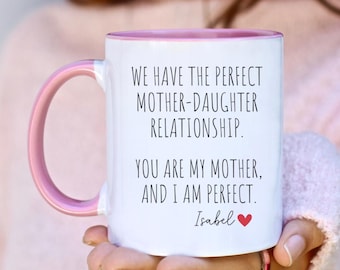 May include: White ceramic mug with a pink rim and handle. The mug has black text that reads "We have the perfect mother-daughter relationship. You are my mother, and I am perfect. Isabel" with a red heart.