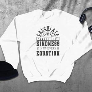 May include: White long-sleeved sweatshirt with a black graphic design that says "Calculate Kindness into Every Equation" with a protractor and math symbols.