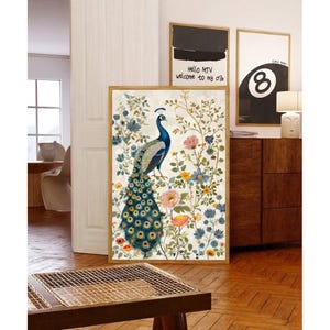 May include: A framed art print featuring a peacock with a vibrant tail, surrounded by colorful flowers and foliage. The artwork is set against a cream background and framed in a light wood. Two other framed prints are visible, one with the text "Hello MTV welcome to my ofs".