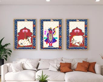 May include: Three framed art prints with Indian-inspired illustrations. Each features a central figure or scene: a cow, a deity, and a cow with a calf. The frames have a blue floral border and a red arch design.