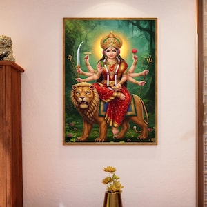 Peut inclure: Une œuvre d'art encadrée représente une divinité à plusieurs bras chevauchant un lion. La figure porte une couronne et des vêtements rouges, tenant divers objets. L'arrière-plan présente une forêt luxuriante avec une lumière rayonnante émanant de derrière la tête de la divinité.