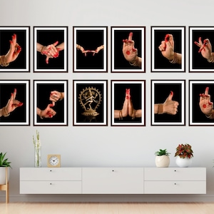 May include: A collection of framed art prints featuring hands in various mudras, or symbolic gestures, against a black background. The hands are adorned with gold bangles and red nail polish. The artwork is displayed above a white cabinet with plants and decor.