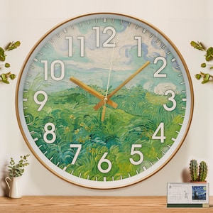 May include: A round wall clock with a gold frame and white face. The clock face features a painting of a green landscape with white clouds and gold hour and minute hands. The numbers 1 through 12 are printed in white around the edge of the clock face.