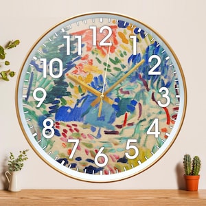 May include: A circular wall clock with a gold-coloured frame. The clock face displays a vibrant abstract painting in blue, red, yellow, and green. White numerals indicate the hours. The clock hands are gold-coloured.