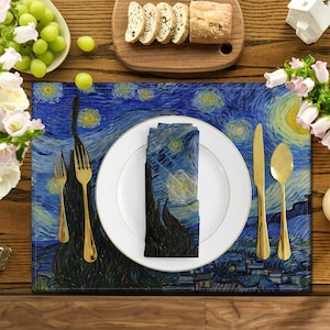 Può includere: Un runner da tavolo blu e giallo con una stampa de La Notte Stellata di Van Gogh. Il runner è apparecchiato con un piatto bianco, posate d'oro e un tovagliolo abbinato.
