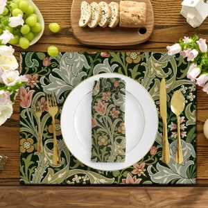 May include: A green and white floral patterned placemat with a white plate, gold cutlery, and a matching napkin. The placemat is set on a wooden table.