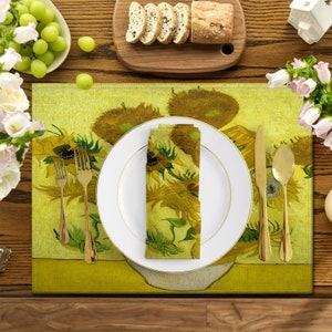 Può includere: Una tavola apparecchiata con un sottopiatto, un tovagliolo e un piatto decorati con un dipinto di girasoli. Posate dorate, un tagliere con pane a fette e una ciotola di uva verde completano la composizione. Il tavolo è in legno.