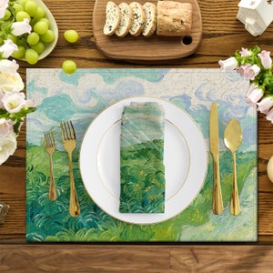 Può includere: Un piatto bianco con un bordo dorato è posto su un sottopiatto verde e blu con un dipinto di un campo d'erba e nuvole. Due forchette dorate e un coltello dorato sono posizionati a sinistra del piatto. Un tovagliolo piegato con un dipinto simile è posto sul piatto.