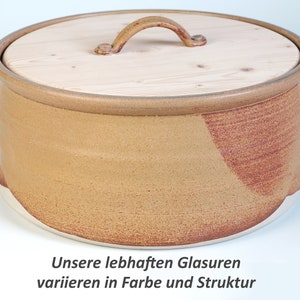 Op de afbeelding: Een handgemaakte keramische container met een houten deksel. De container is bruin met een roodbruin accent en een witte basis. Het deksel heeft een houten handvat. De tekst onderaan luidt: "Unsere lebhaften Glasuren variieren in Farbe und Struktur."