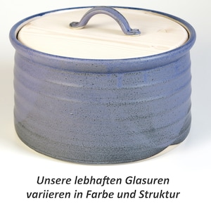Könnte beinhalten: Ein blauer Keramik-Brotbehälter mit einem Holzdeckel und einem Griff. Der Deckel hat eine natürliche Holzoptik. Der Behälter hat eine strukturierte Glasur.