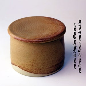 May include: A ceramic butter dish with a lid. The dish is a light brown colour with a darker brown glaze. The lid has a slightly raised rim.