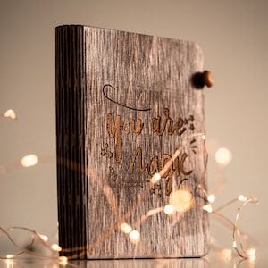 Könnte beinhalten: Ein Holzjournal mit den Worten "You are magic" auf der Vorderseite eingraviert. Das Journal ist von einer Lichterkette umgeben.