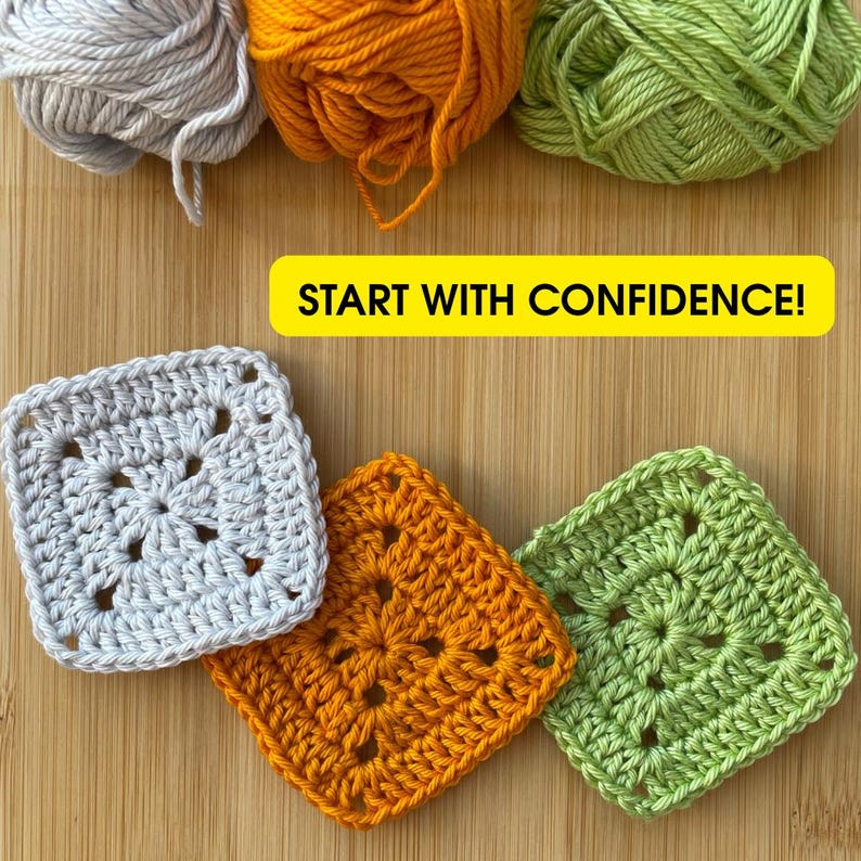 K&ouml;nnte beinhalten: Auf einer Holzoberfl&auml;che liegen drei geh&auml;kelte Granny Squares in Grau, Orange und Gr&uuml;n, dar&uuml;ber passende Wollkn&auml;uel. Der Text "START WITH CONFIDENCE!" steht in einem gelben Rechteck.