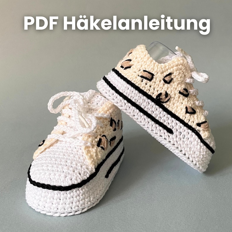 Babyschuhe mit beige-schwarzem Muster in der Hand präsentiert
