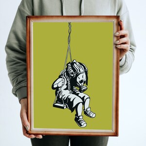 May include: Framed art print featuring a black and white illustration of a figure wearing a gas mask on a swing. The artwork is set against a lime green background and framed in a brown wooden frame. The image evokes themes of environmental awareness.