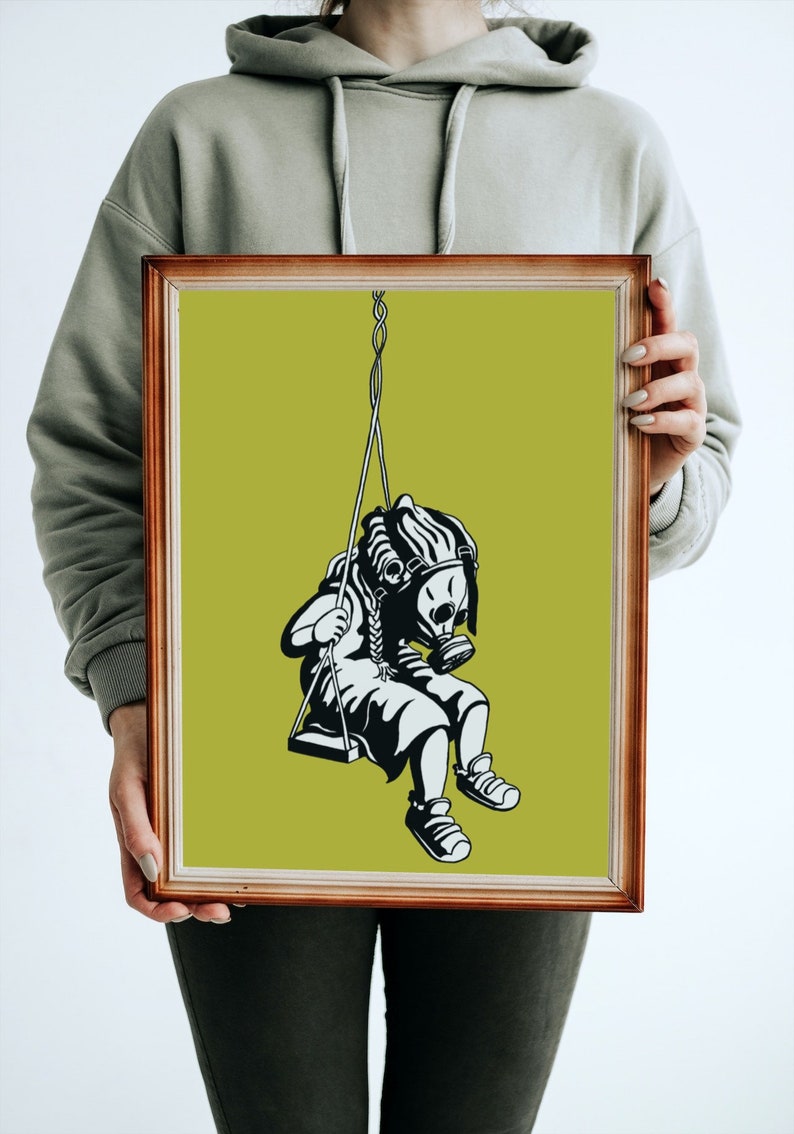 May include: Framed art print featuring a black and white illustration of a figure wearing a gas mask on a swing. The artwork is set against a lime green background and framed in a brown wooden frame. The image evokes themes of environmental awareness.